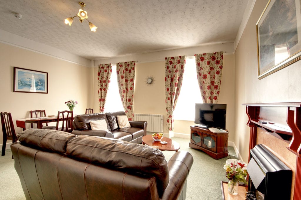 Living room with brown leather sofas, tv and red floral curtains