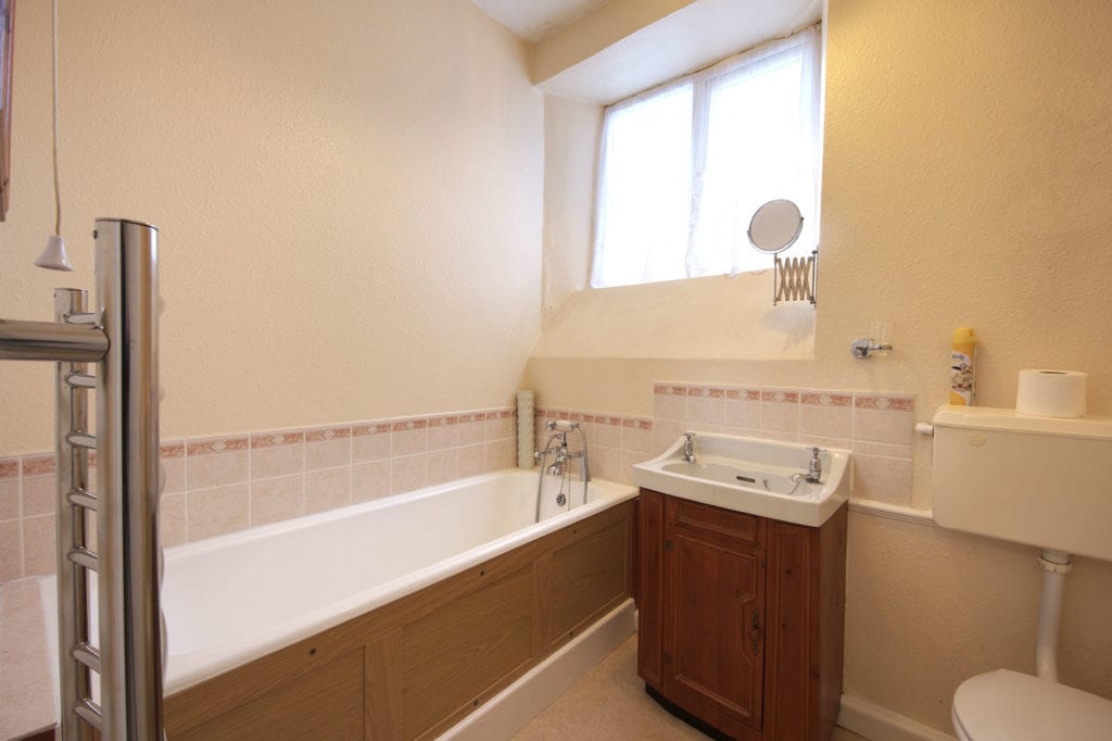 Light bathroom with wood panelled bath, sink and toilet