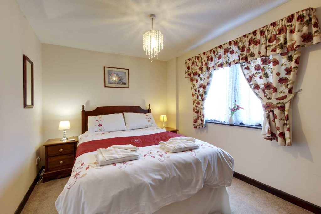 Bedroom containing a double bed with red flower covers and curtains plus wooden bedside table