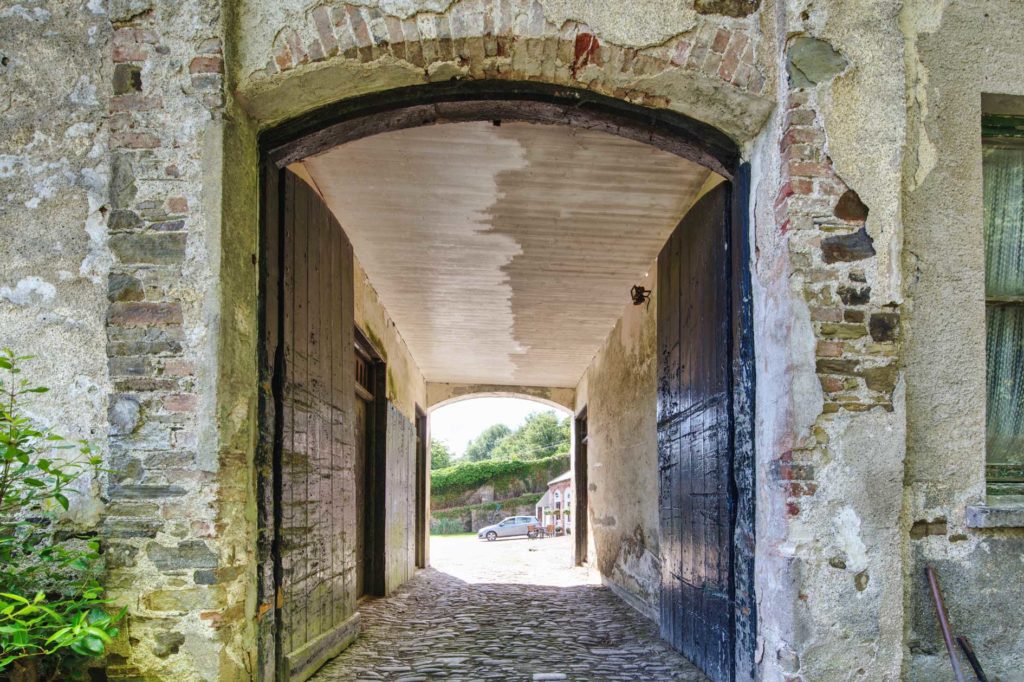View through old stone arch with dark wooden doors and cobbled floor