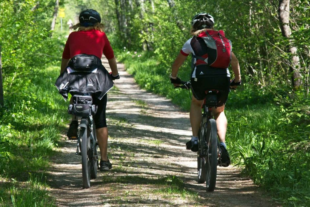 two people in helmets and red tops cycling down country tree and grass lined track