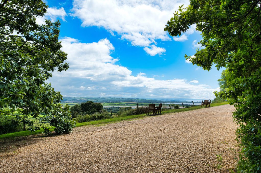 Gravel driveway with tress and distance countryside views and blue sky